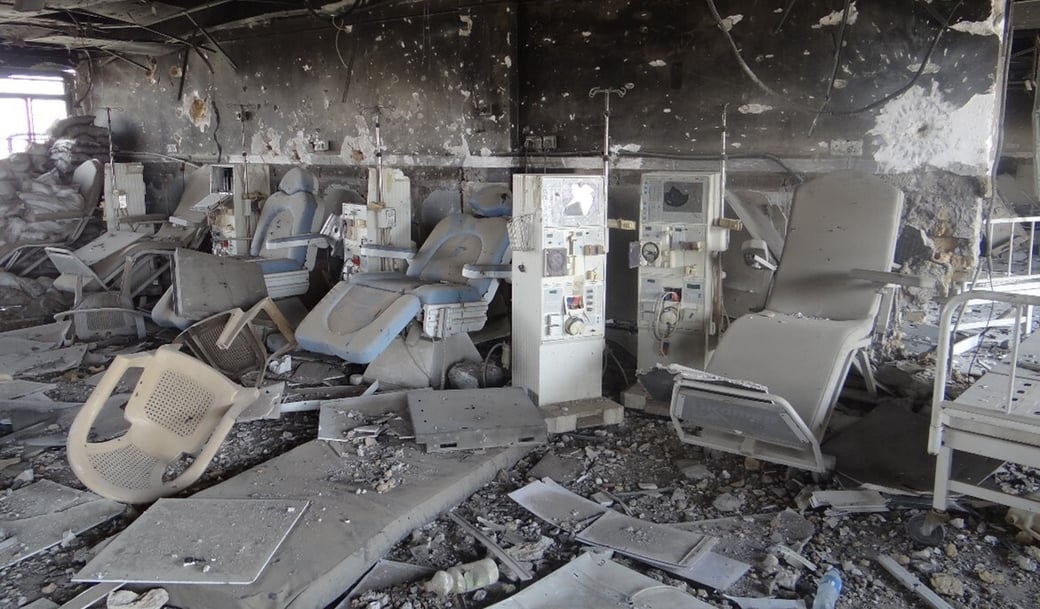 A dialysis unit in Ibn Sina General Hospital, Mosul, with shattered equipment, debris, and scorched walls showing signs of severe damage.