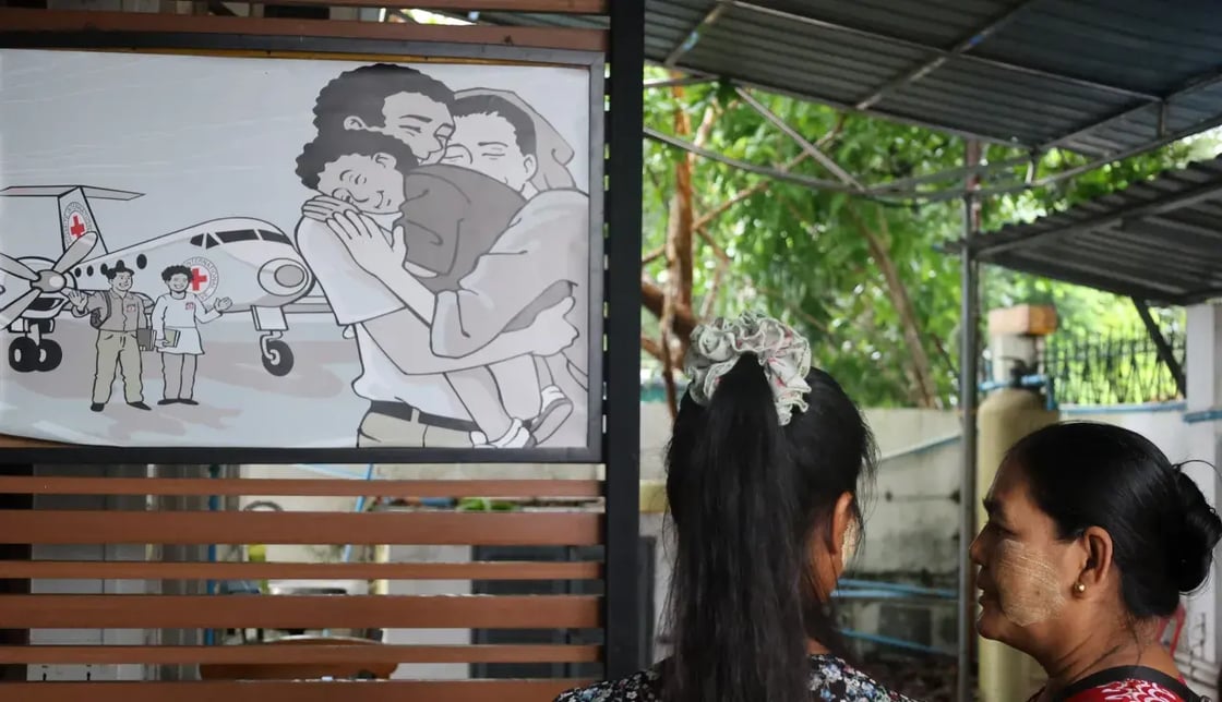 In Myanmar, two women look at a poster showing a family reunion beside an ICRC plane, symbolizing hope for families of the missing.