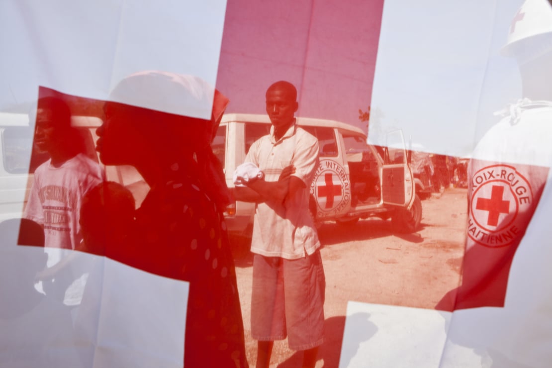 A man standing behind a red cross flag.