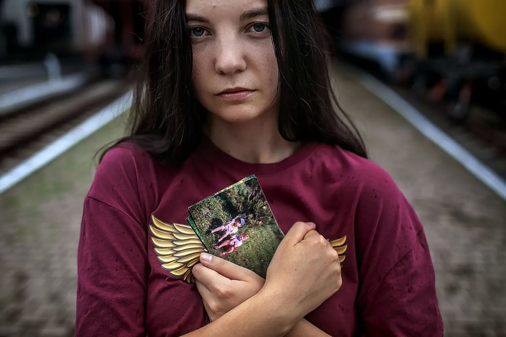 Olena holds a childhood photo of herself and her brother Andrii close to her chest at a train station in Kyiv.